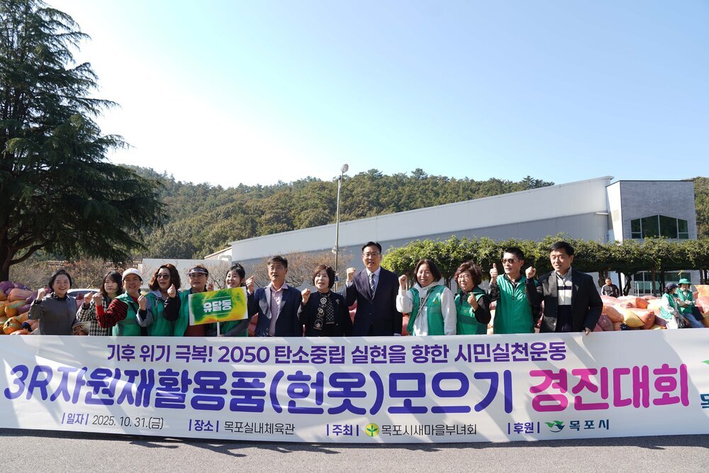 '3R 자원재활용품(헌옷) 모으기 경진대회' 현수막 앞에서 유달동 참가자들이 기념사진을 촬영하고 있다. 현수막 뒤로 수집된 헌옷 꾸러미들이 가득 쌓여 있다.