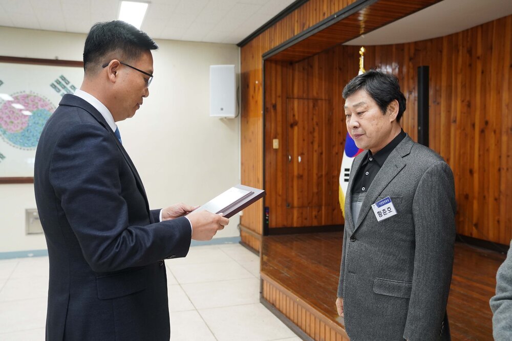 2월 정례조회에 정장을 입고 안경을 낀 남성이 회색 정장 자켓을 입은 황춘호에게 패를 수여하고 있다.