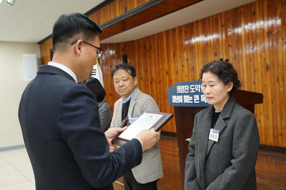 2월 정례조회에 정장을 입고 안경을 낀 남성이 짙은 회색 코트 자켓을 입은 차미경에게 패를 수여하고 있다.