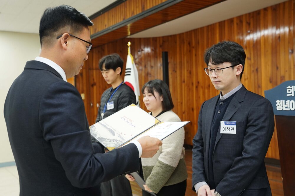 2월 정례조회에 정장을 입고 안경을 낀 남성이 검전색 정장수트를 입은 이창민에게 패를 수여하고 있다.