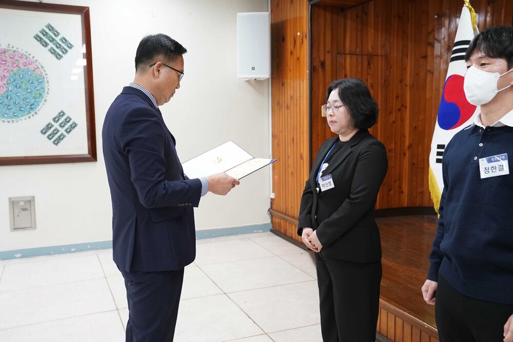 4월 정례조회에 정장을 입고 안경을 낀 남성이 검은정장을 입은 박신영에게 패를 수여하고 있다