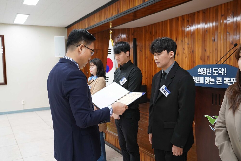 4월 정례조회에 정장을 입고 안경을 낀 남성이 검은정장을 입은 고해광에게 패를 수여하고 있다