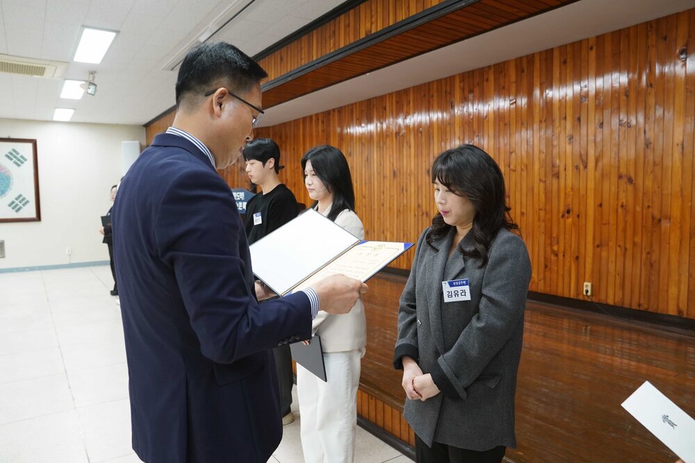 4월 정례조회에 정장을 입고 안경을 낀 남성이 회색 자켓을 입은 김유라에게 패를 수여하고 있다