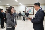 2026년 상반기 4급이하 정기인사로 정장을 입은 남성이 실내 행사장에서 한 여성에게 상장을 전달하며 내용을 읽고 있고, 여성은 회색 재킷을 입고 두 손을 모은 상태로 서 있으며 뒤쪽에는 참석자들이 줄지어 서서 행사를 지켜보고 있다.