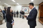 2026년 상반기 4급이하 정기인사로 정장을 입은 남성이 실내 행사장에서 한 여성에게 상장을 전달하며 내용을 읽고 있고, 여성은 검은 상의를 입고 두 손을 모은 상태로 서 있으며 뒤쪽에는 참석자들이 줄지어 서서 행사를 지켜보고 있다.