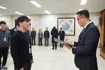 2026년 상반기 4급이하 정기인사로 정장을 입은 남성이 실내 행사장에서 한 남성에게 상장을 전달하며 내용을 읽고 있고, 남성은 검은 니트를 입은 채 두 손을 모은 상태로 서 있으며 뒤쪽에는 참석자들이 줄지어 서서 행사를 지켜보고 있다.