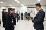2026년 상반기 4급이하 정기인사로 정장을 입은 남성이 실내 행사장에서 한 여성에게 상장을 전달하며 내용을 읽고 있고, 여성은 검은 상의를 입고 사원증을 착용한 채 두 손을 모은 상태로 서 있으며 뒤쪽에는 참석자들이 줄지어 서서 행사를 지켜보고 있다.