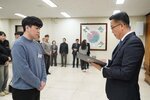 2026년 상반기 4급이하 정기인사로 정장을 입고 안경을 쓴 남성이 실내 행사장에서 한 남성에게 상장을 전달하며 내용을 읽고 있고, 남성은 회색 니트를 입고 두 손을 모은 채 서 있으며 뒤쪽에는 참석자들이 줄지어 서서 행사를 지켜보고 있다.