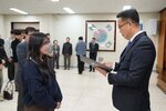 2026년 상반기 4급이하 정기인사로 정장을 입고 안경을 쓴 남성이 실내 행사장에서 한 여성에게 상장을 전달하며 내용을 읽고 있고, 여성은 남색 맨투맨을 입고 두 손을 모은 채 서 있으며 뒤쪽에는 참석자들이 줄지어 서서 행사를 지켜보고 있다.