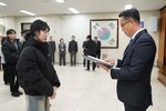 2026년 상반기 4급이하 정기인사로 정장을 입고 안경을 쓴 남성이 실내 행사장에서 한 여성에게 상장을 전달하며 내용을 읽고 있고, 여성은 검은 패딩을 입고 안경을 착용한 채 두 손을 모은 채 서 있으며 뒤쪽에는 참석자들이 줄지어 서서 행사를 지켜보고 있다.