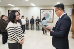 2026년 상반기 4급이하 정기인사로 정장을 입고 안경을 쓴 남성이 실내 행사장에서 한 여성에게 상장을 전달하며 내용을 읽고 있고, 여성은 줄무늬 니트를 입고 두 손을 모은 채 서 있으며 뒤쪽에는 참석자들이 줄지어 서서 행사를 지켜보고 있다.