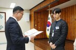2월 정례조회에 정장을 입고 안경을 낀 남성이 검은색바지에 검은색 경랼패딩을 입은 임성훈에게 패를 수여하고 있다.