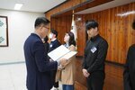 4월 정례조회에 정장을 입고 안경을 낀 남성이 검정색 셔츠를 입은 박정우에게 패를 수여하고 있다