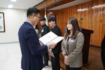 4월 정례조회에 정장을 입고 안경을 낀 남성이 짙은 오트밀색 자켓을 입은 오지인에게 패를 수여하고 있다